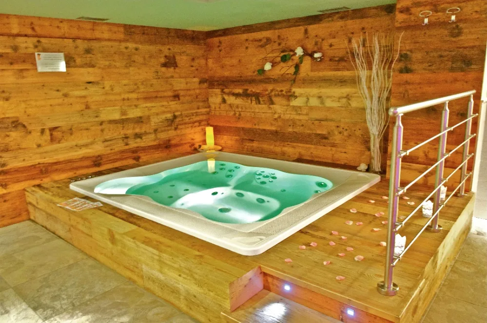 Vasca idromassaggio in legno della spa con acqua verde e petali di rosa
