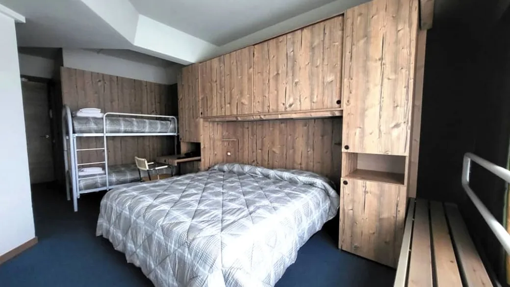 Camera con letto matrimoniale e letto a castello, arredi in legno chiaro di montagna