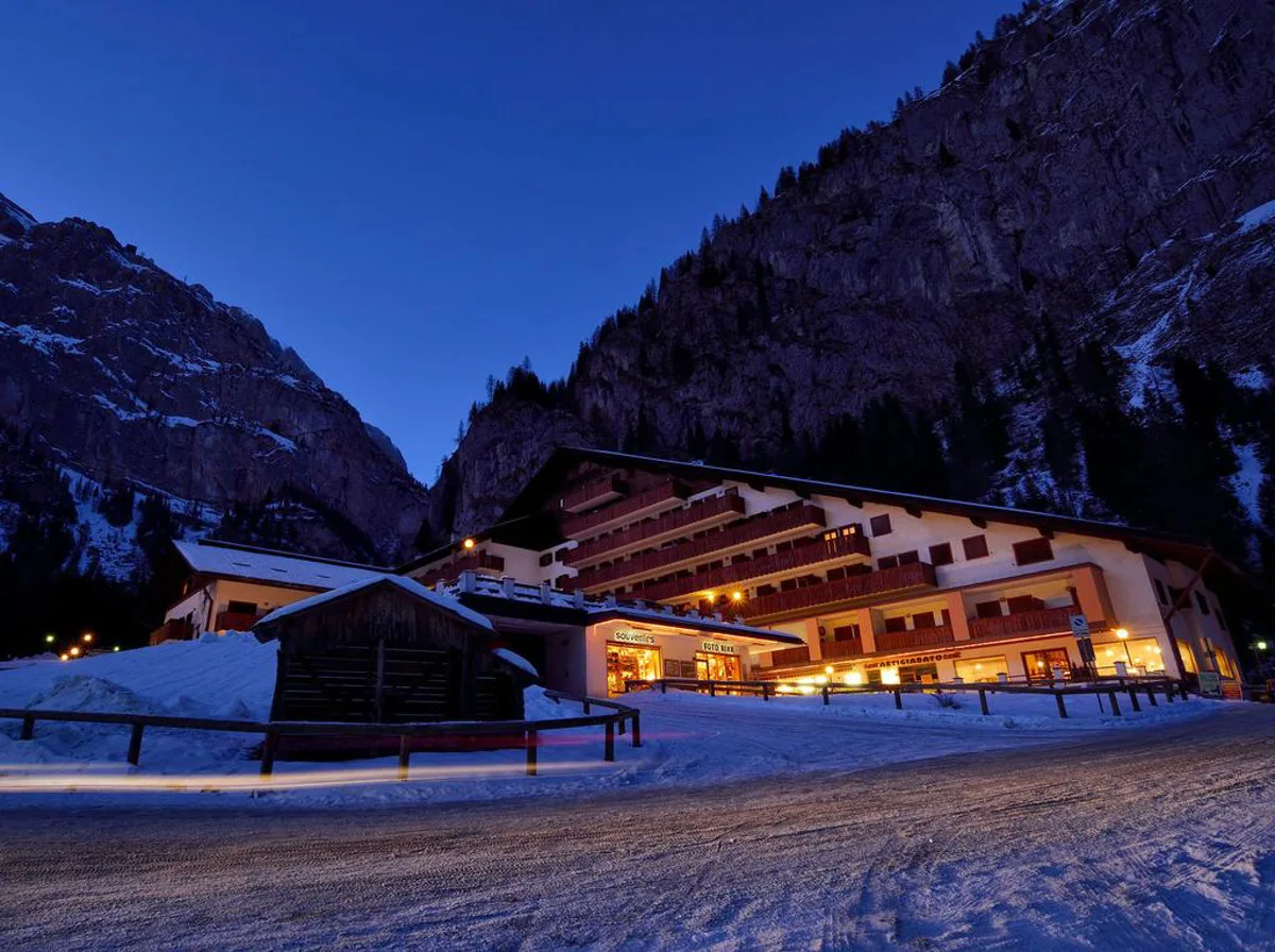 Hotel illuminato di sera nella valle innevata, con negozi e montagne scure sullo sfondo