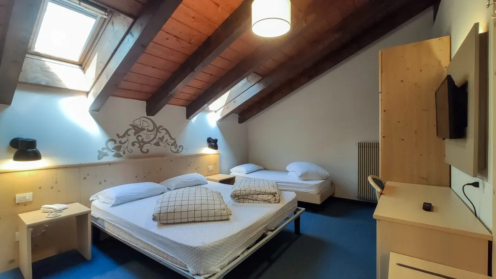 Camera mansardata con travi in legno a vista, letti e lucernario