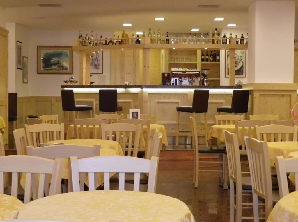 Bar interno dell'hotel con sgabelli, tavoli con tovaglie gialle e ampia scelta di bottiglie