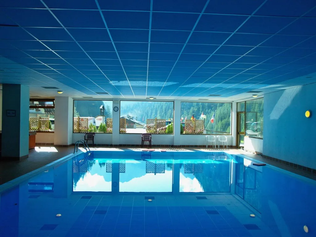 Piscina coperta con soffitto azzurro e grandi vetrate affacciate sul paesaggio montano