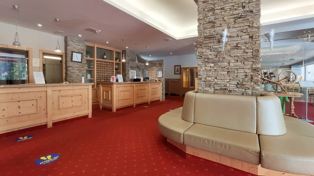 Reception dell'hotel con bancone in legno, colonna in pietra e divano circolare su moquette rossa