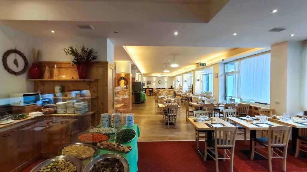 Sala ristorante con buffet di verdure e contorni in primo piano e tavoli apparecchiati
