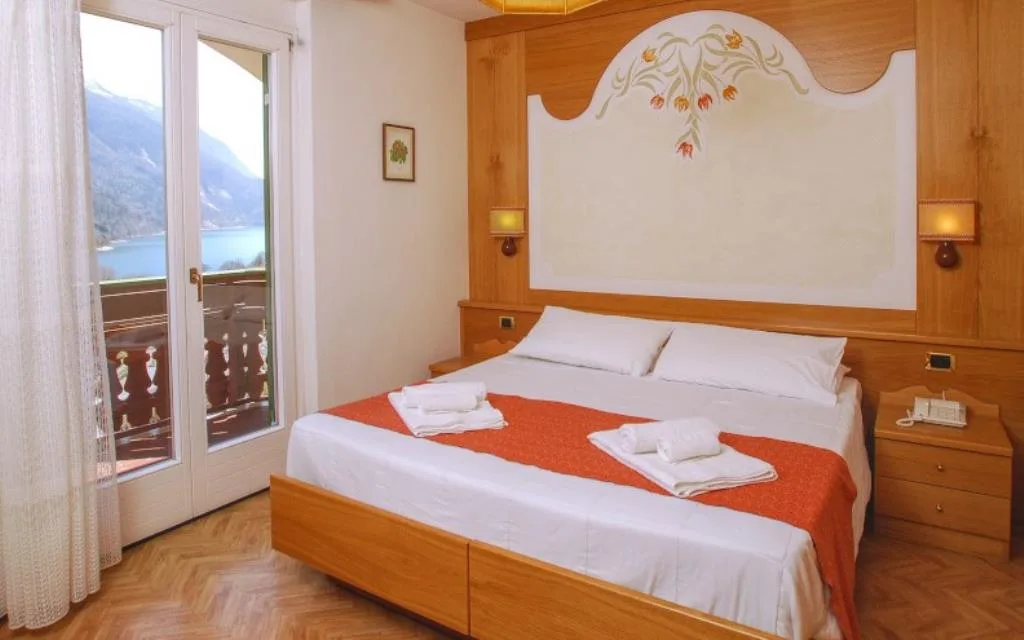 Camera matrimoniale con arredi in legno, testata decorata e balcone con vista sul lago