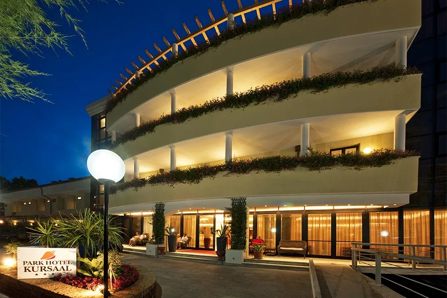 Ingresso illuminato del Park Hotel Kursaal di sera con insegna e giardino