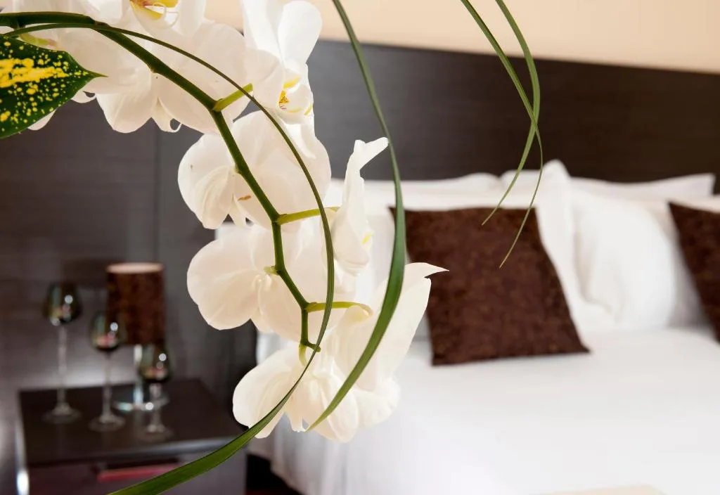 Dettaglio di camera con orchidee bianche in primo piano e letto sullo sfondo