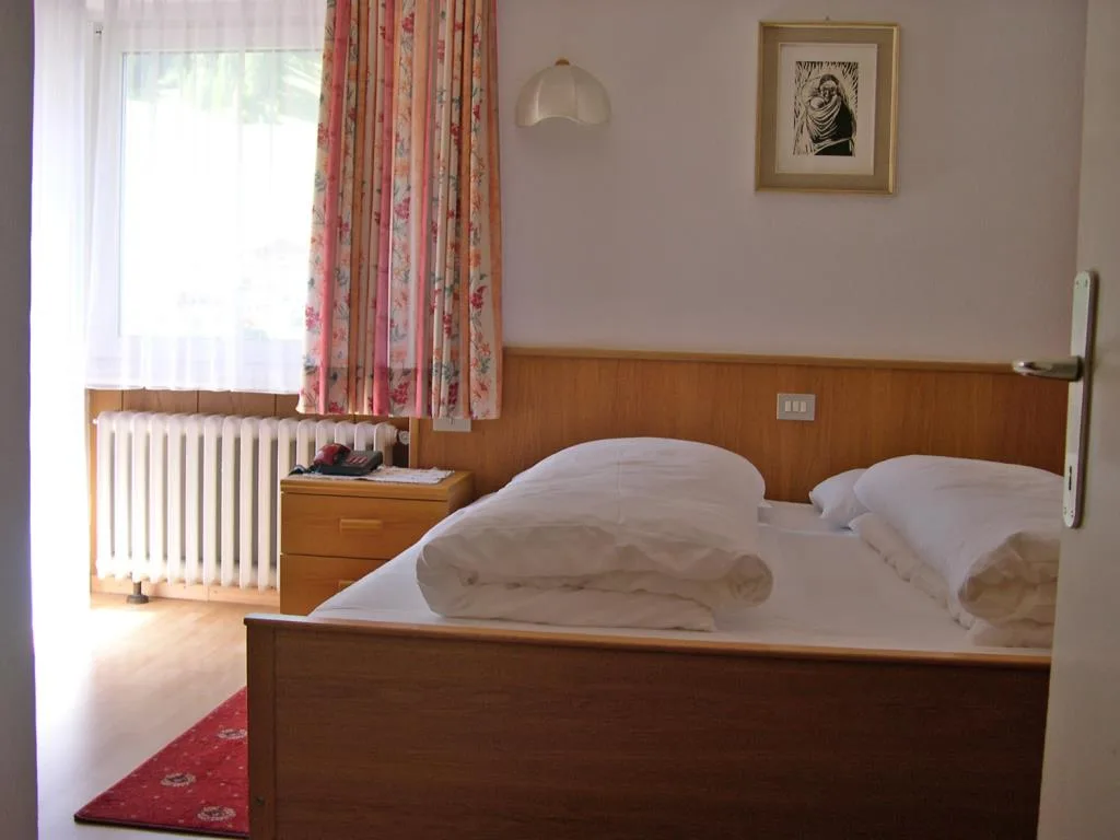 Camera da letto con letto matrimoniale, finestra con tende floreali e radiatore