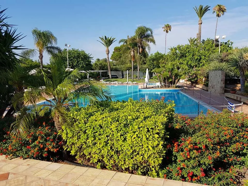 Piscina immersa nel giardino con siepi fiorite e palme lussureggianti