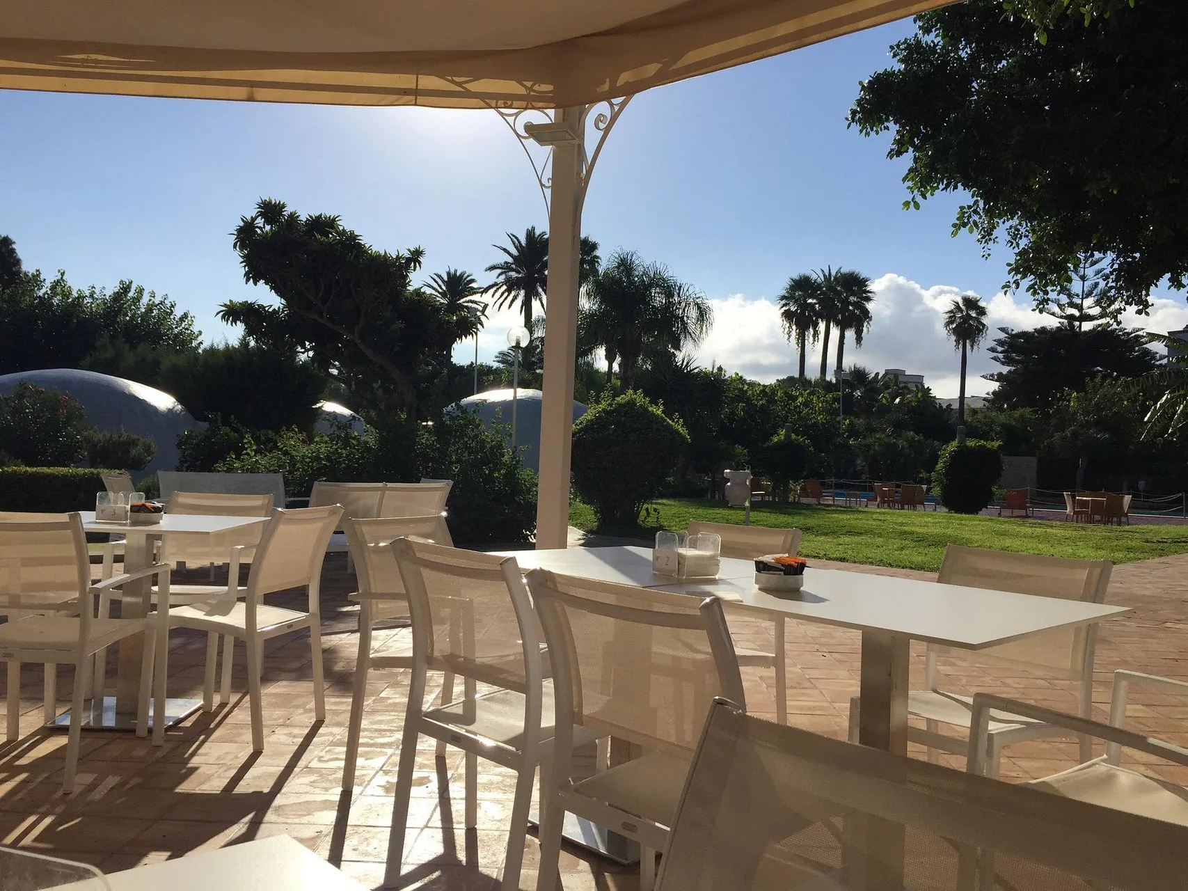 Terrazza ristorante all'aperto con tavoli e sedie bianche affacciata sul giardino
