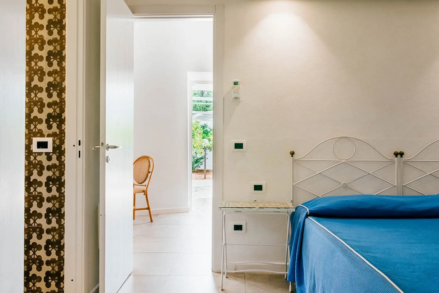 Dettaglio di camera con letto, piastrelle decorative e vista sul corridoio