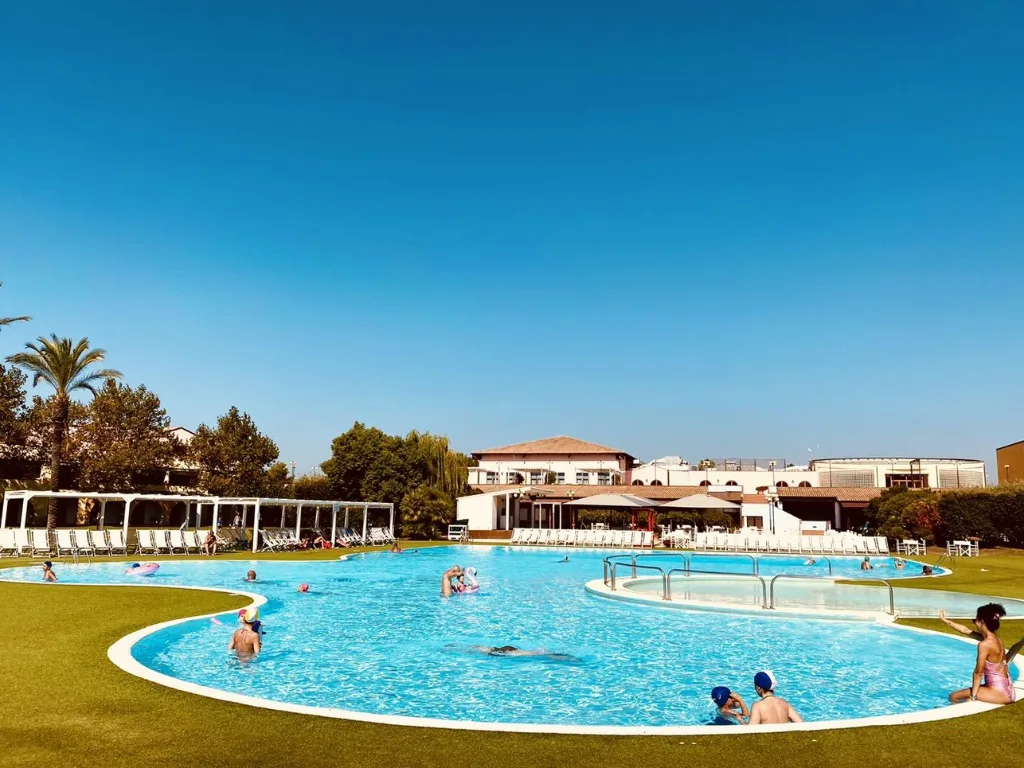 Grande piscina curvilinea con bagnanti e prato verde circostante