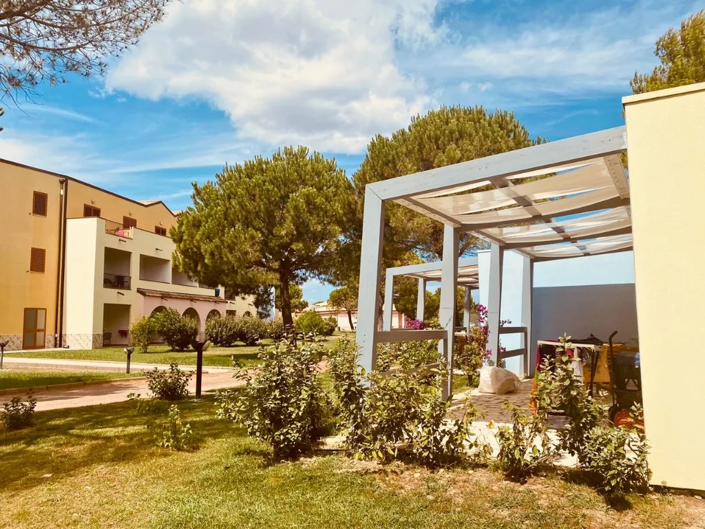 Viale del residence con pergolato, pini e edifici colorati