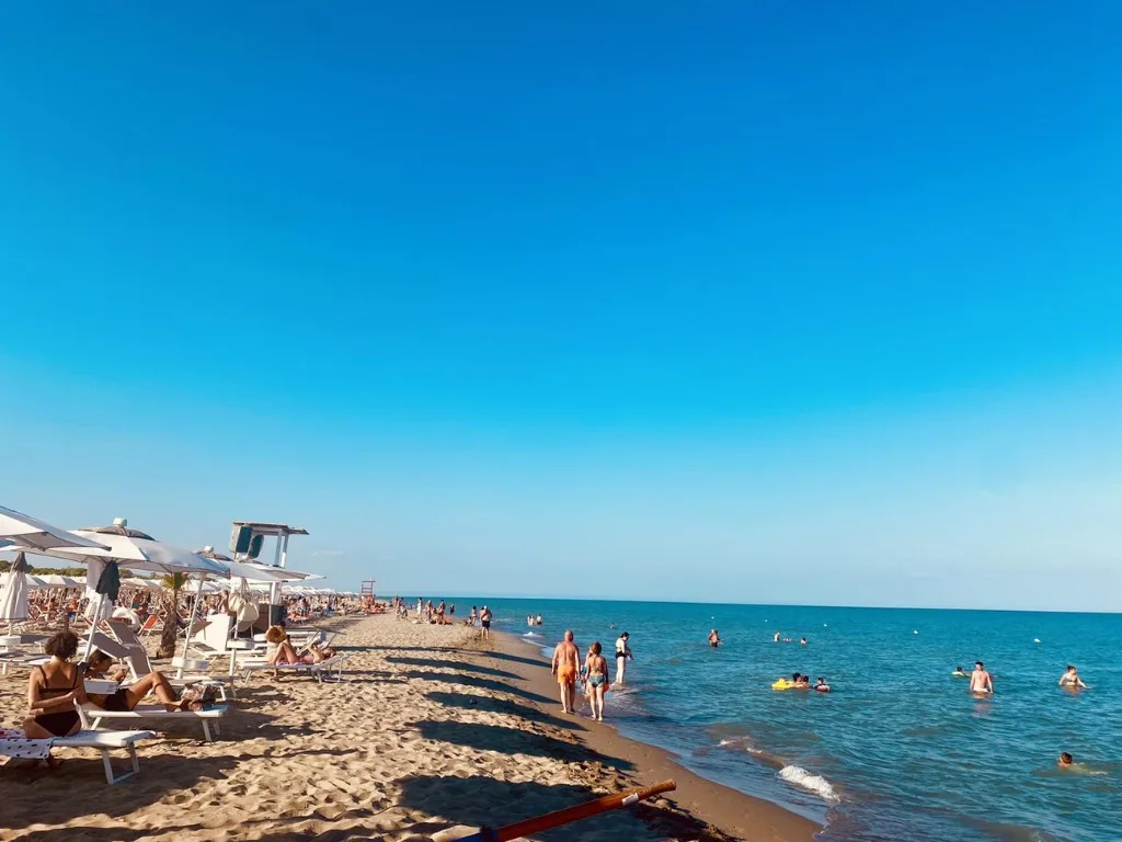 Spiaggia sabbiosa con bagnanti, ombrelloni e mare azzurro