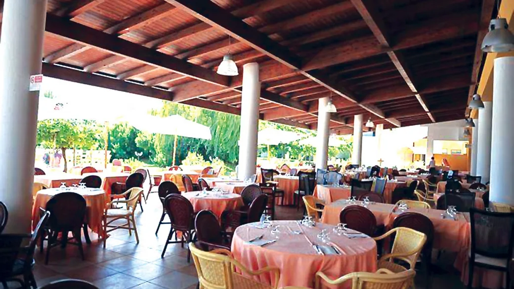Ristorante coperto con tavoli rotondi apparecchiati e vista sul giardino
