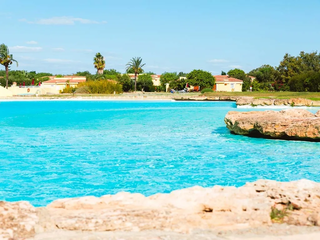 Piscina a laguna con acqua turchese, rocce e vegetazione con ville sullo sfondo