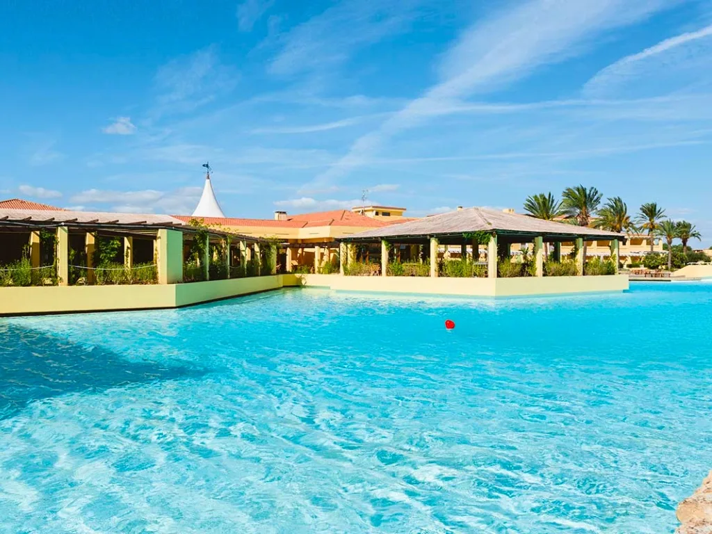 Piscina a laguna con gazebo ombreggiato e vegetazione, edifici del resort sullo sfondo