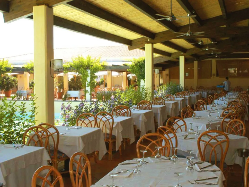 Ristorante all'aperto con tavoli apparecchiati, sedie in vimini e pergola con piante