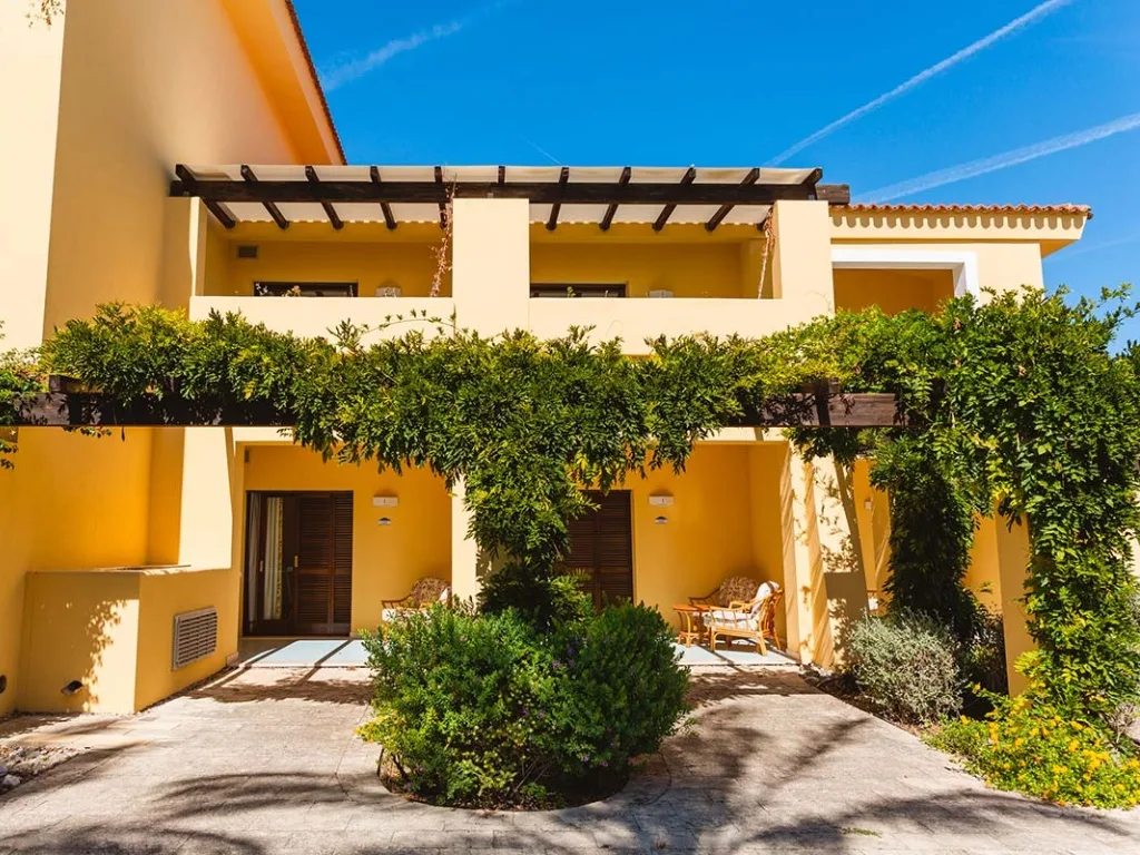 Facciata gialla degli alloggi con pergolato di verde e terrazze sotto un cielo azzurro