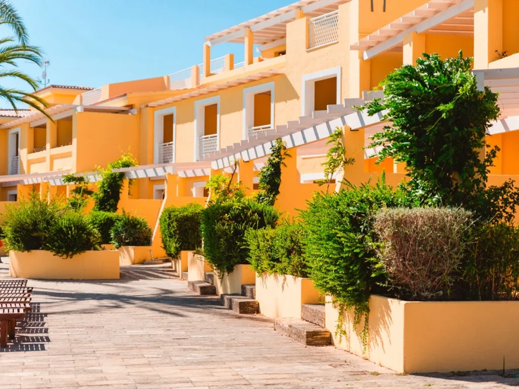 Vialetto tra gli alloggi gialli del resort con pergole bianche e siepi verdi