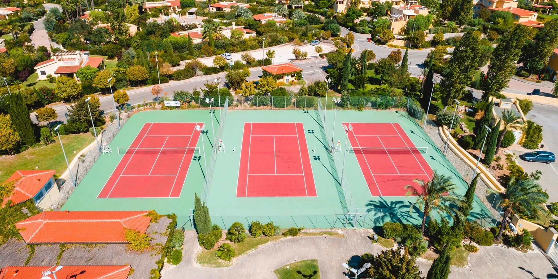 Vista aerea di tre campi da tennis rossi e verdi immersi nel verde del resort