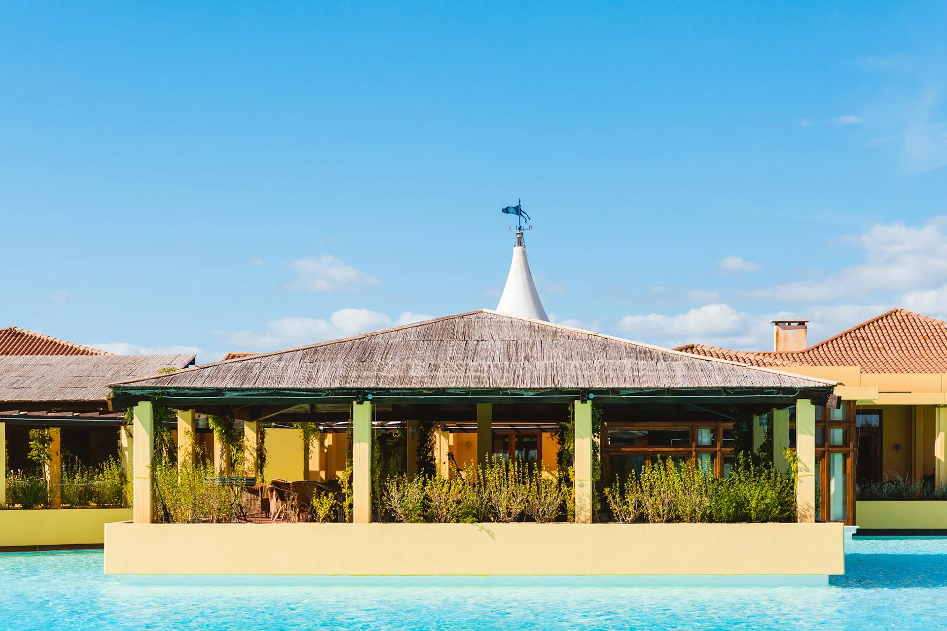 Gazebo con tetto in paglia affacciato sulla piscina e edifici gialli del resort