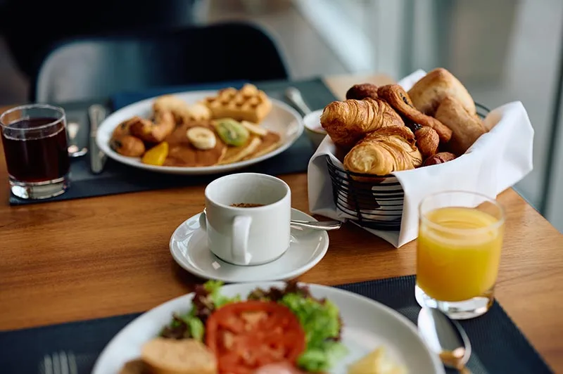 Colazione servita con caffè, cornetti, succo d'arancia e piatti vari su tavolo