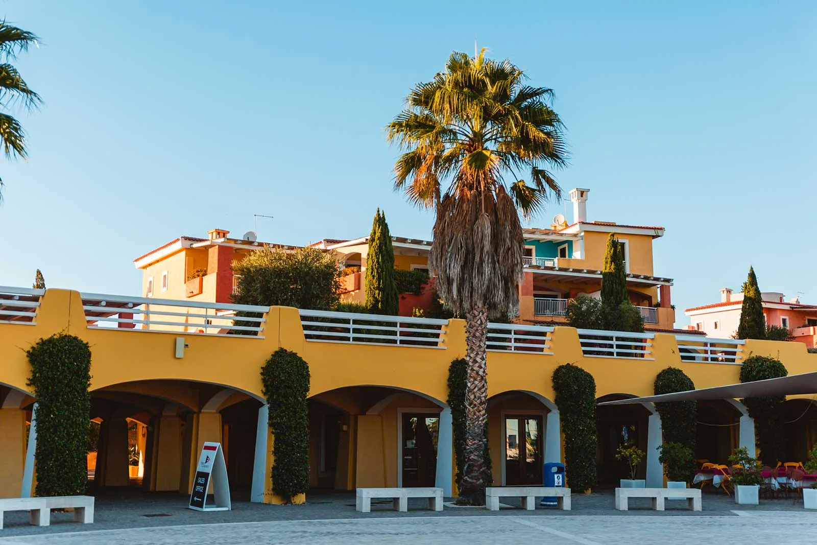 Facciata gialla del resort con portici, palma e edifici colorati sullo sfondo