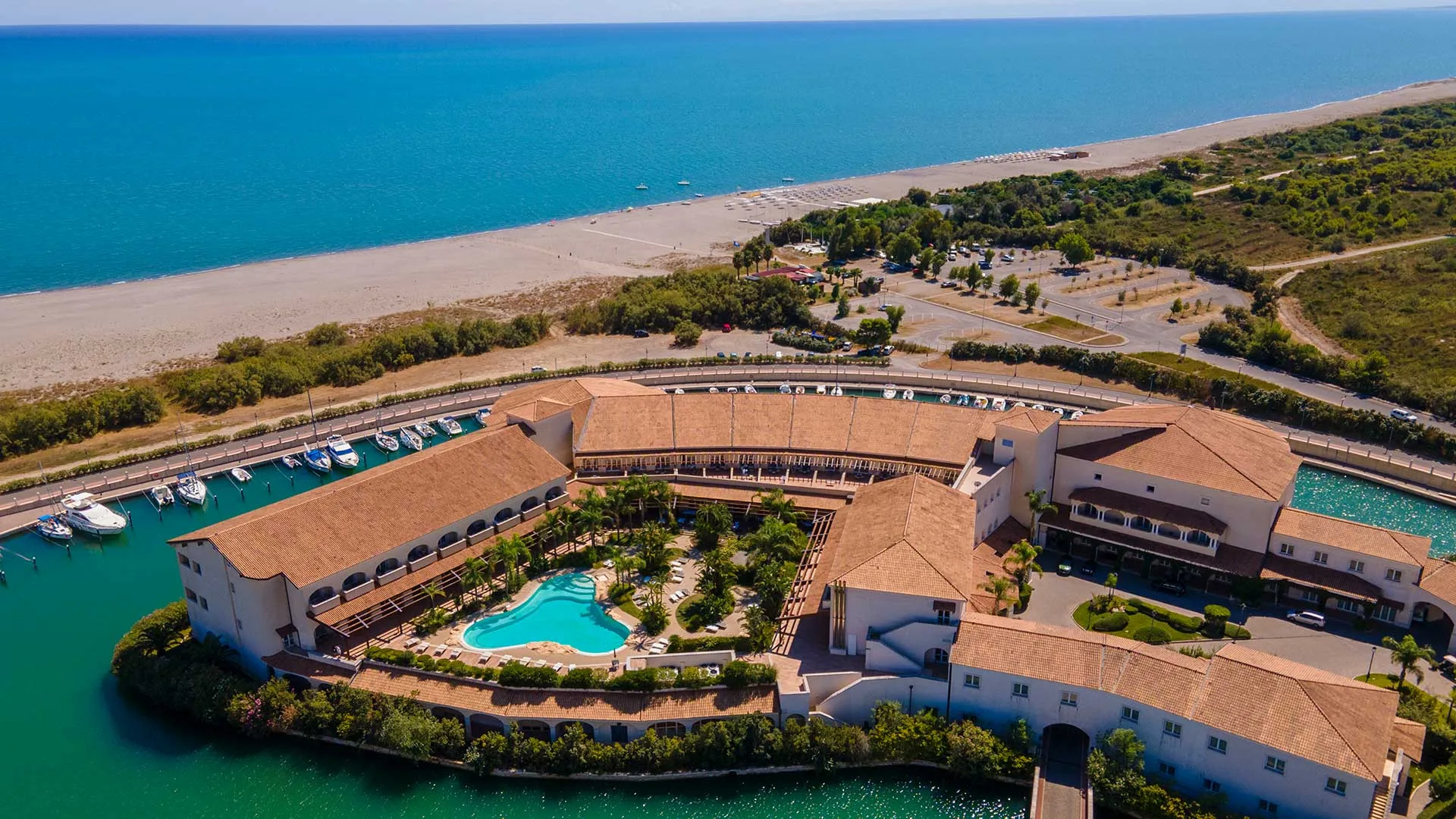 Veduta aerea del resort con piscina, porto turistico, spiaggia sabbiosa e mare cristallino