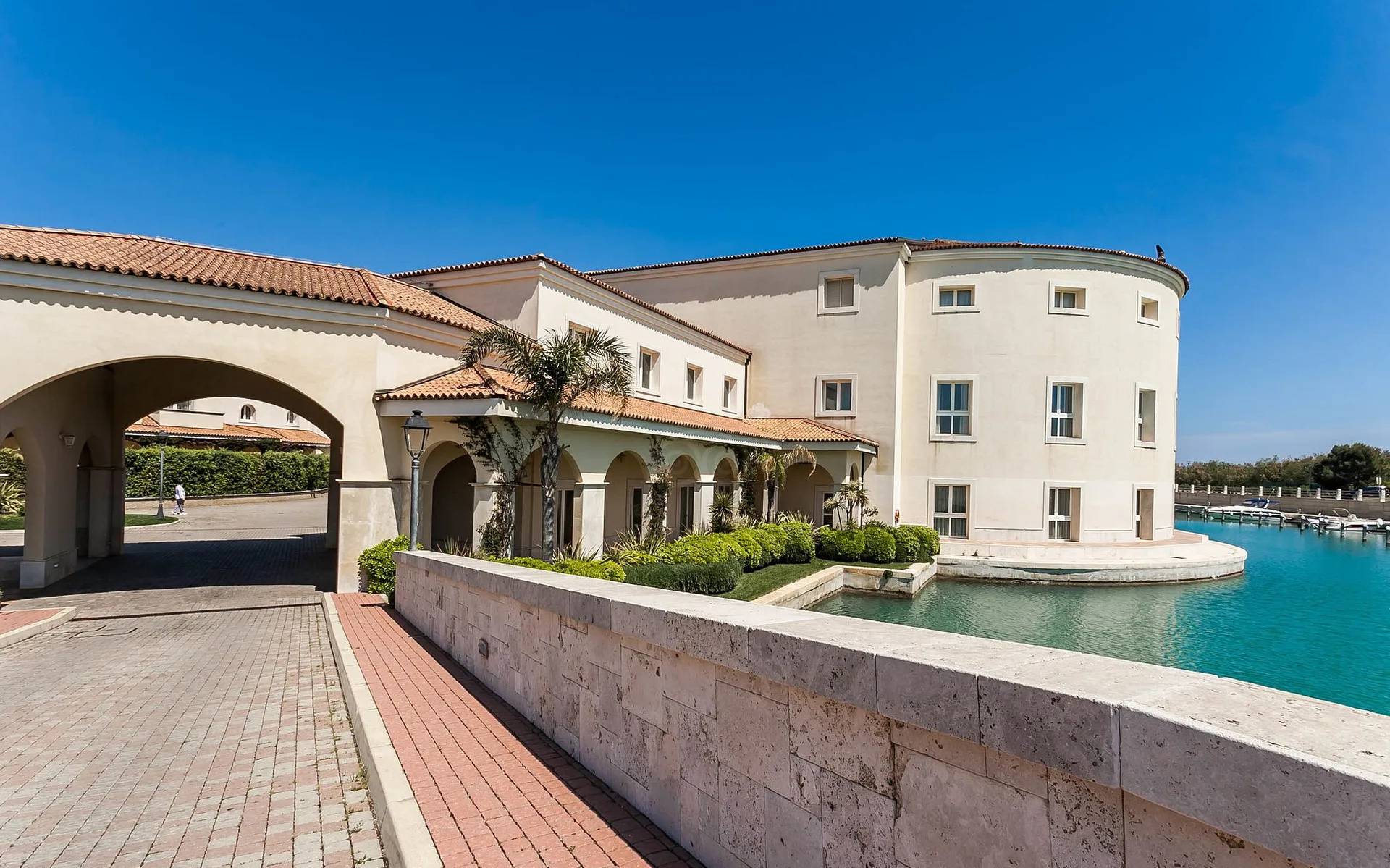 Esterno del resort con arco d'ingresso, portici e edificio circolare affacciato sul canale