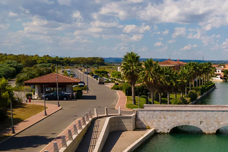 Strada di accesso al resort con casello, palme e canale con ponte sotto cielo nuvoloso