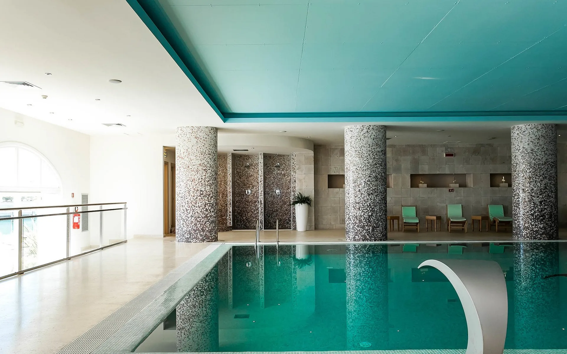Piscina interna con colonne a mosaico, docce e area relax con lettini