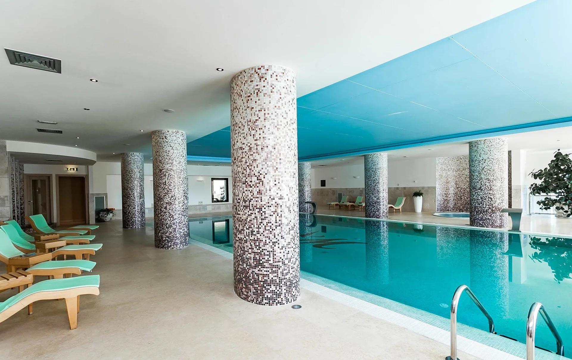 Piscina coperta della spa con colonne a mosaico e lettini in legno lungo il bordo