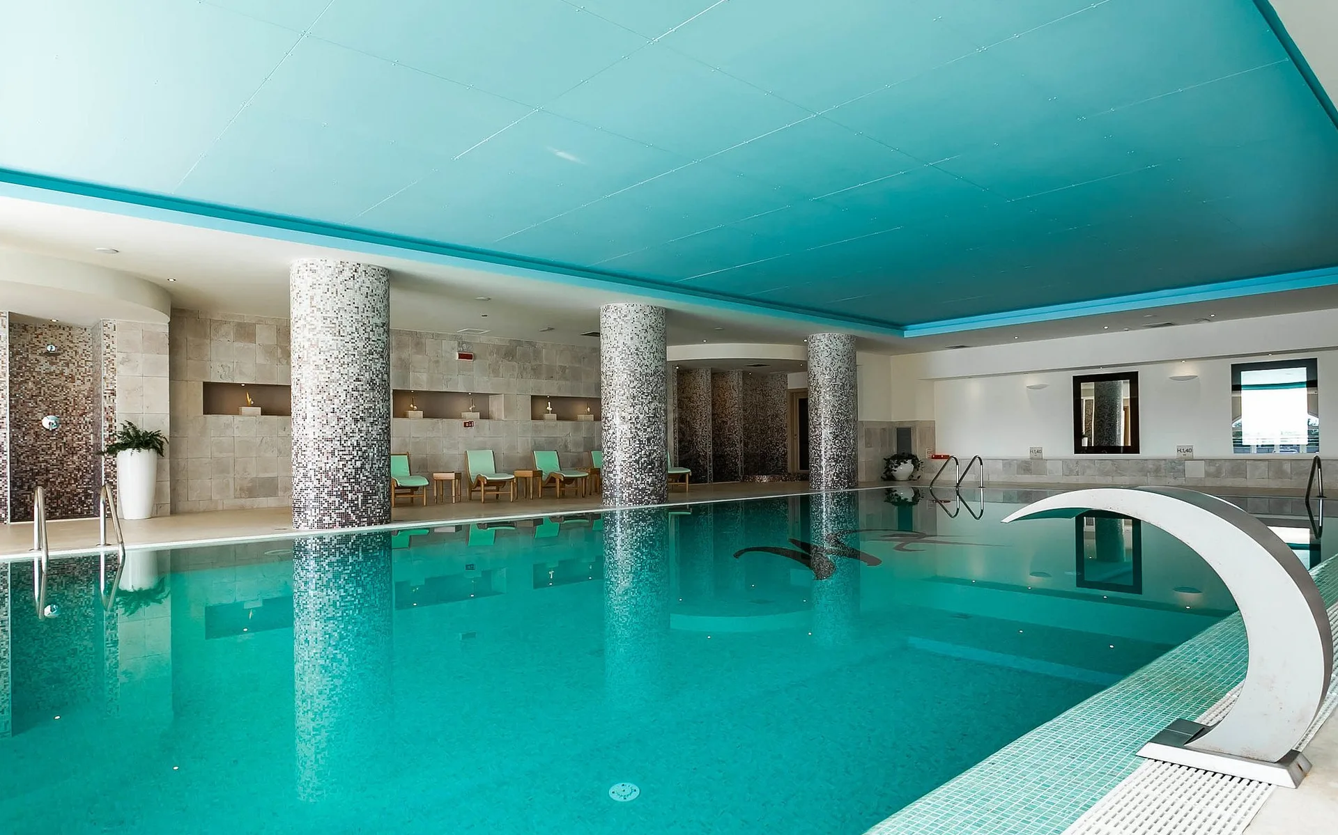 Piscina interna della spa con acqua turchese, colonne a mosaico e lettini relax