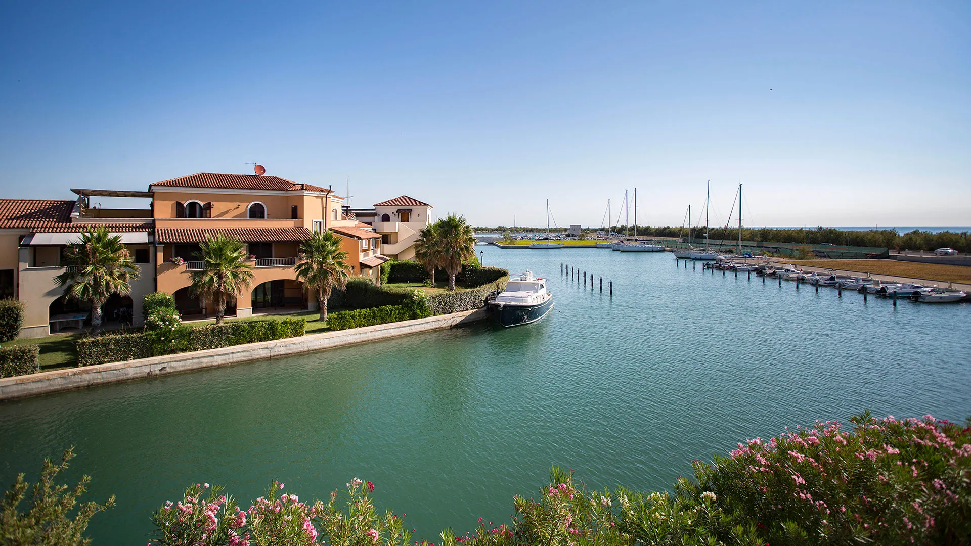 Ville color pastello affacciate sul canale con palme, barca ormeggiata e porto turistico
