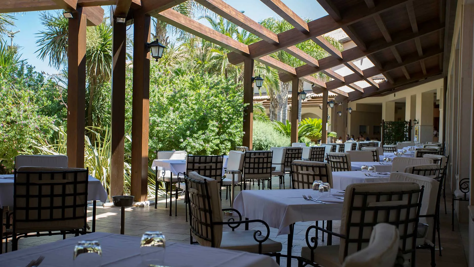 Terrazza ristorante esterna con pergolato in legno, tavoli apparecchiati e vegetazione
