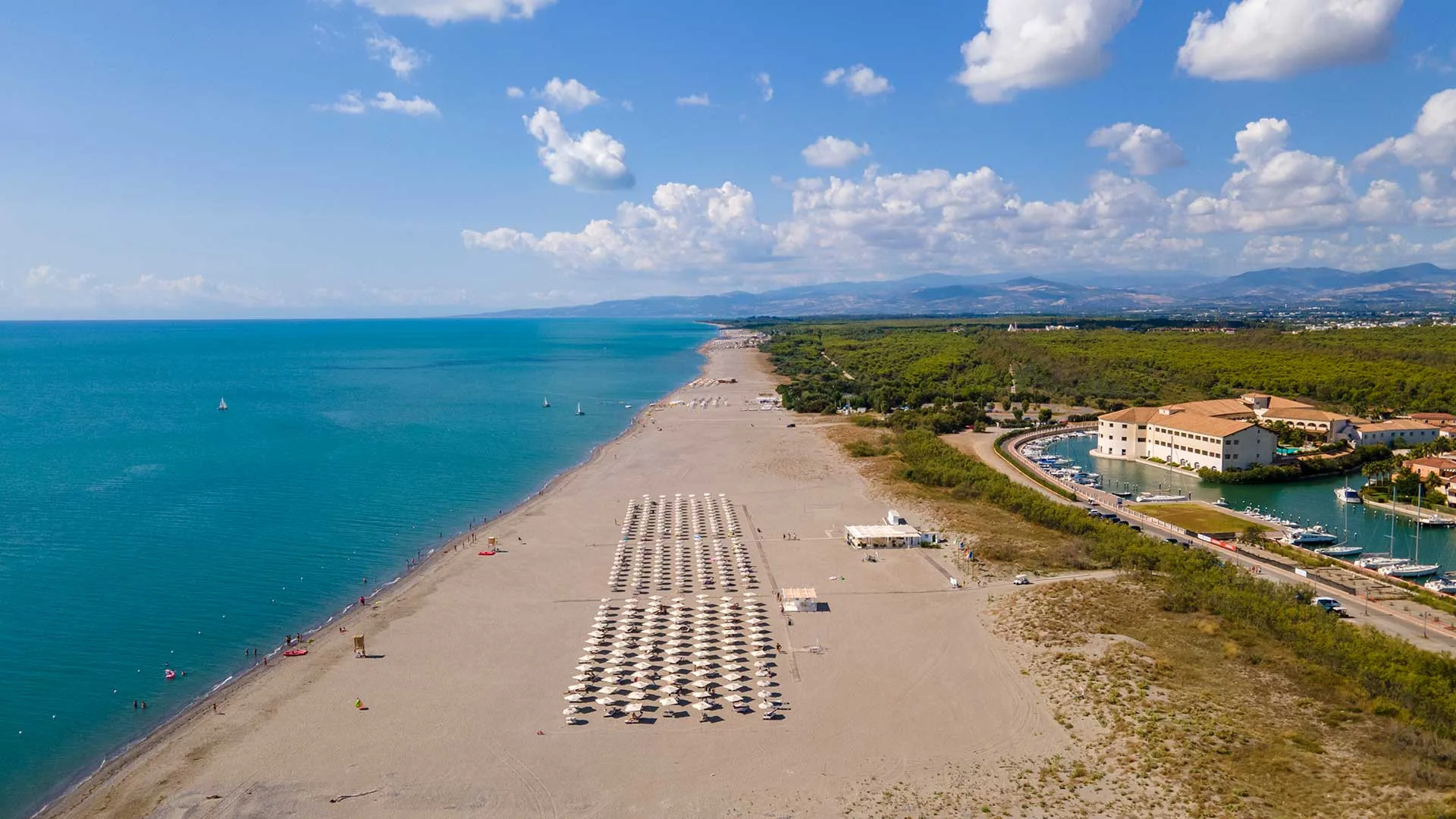 Vista aerea della lunga spiaggia sabbiosa con ombrelloni, mare turchese e resort sullo sfondo