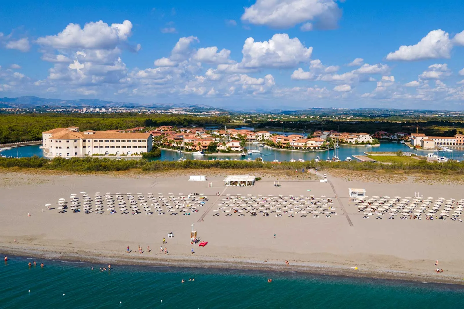 Veduta aerea del resort con spiaggia attrezzata, ombrelloni e villaggio su canali