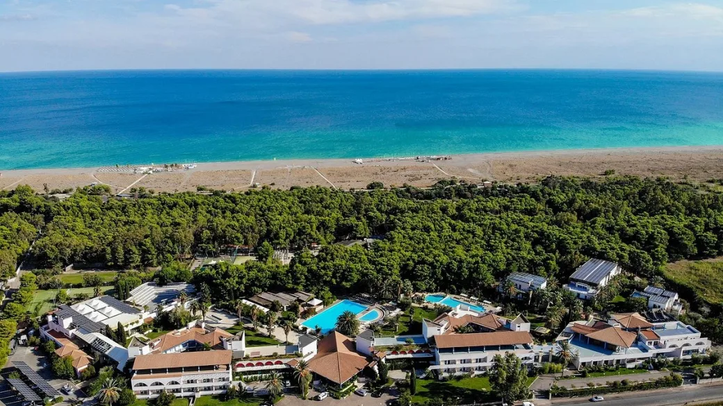 Vista aerea del resort immerso nel verde con piscine e mare blu sullo sfondo