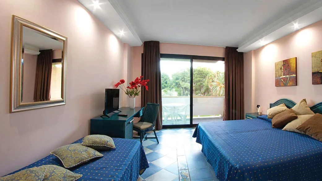 Camera con letto matrimoniale e singolo, copriletti blu, scrivania e balcone vista verde