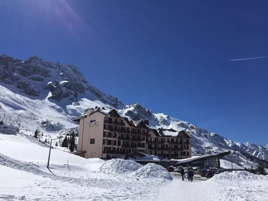 Hotel di montagna innevato ai piedi di cime alpine con cielo azzurro in una giornata di sole