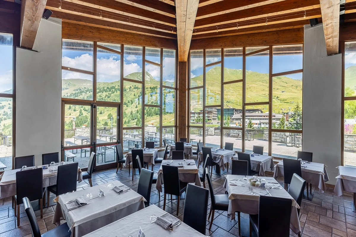 Sala ristorante con travi in legno e vetrate sulle montagne estive