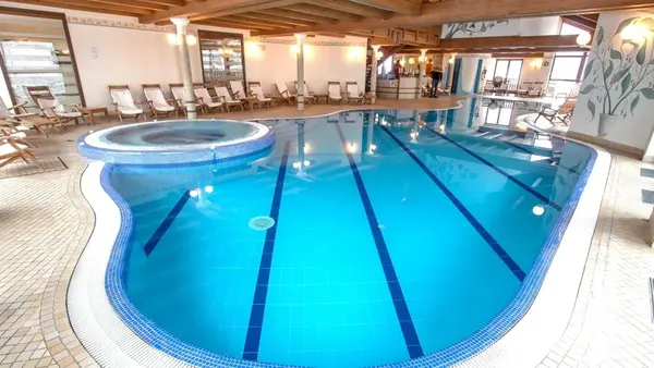Piscina coperta con idromassaggio circolare, lettini e soffitto in legno