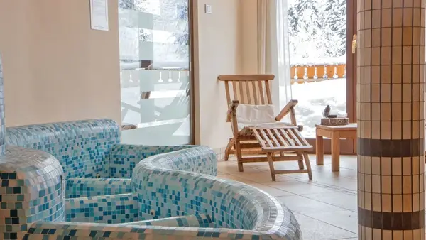 Area relax della spa con poltrone rivestite in mosaico azzurro e lettino in legno vicino alle vetrate