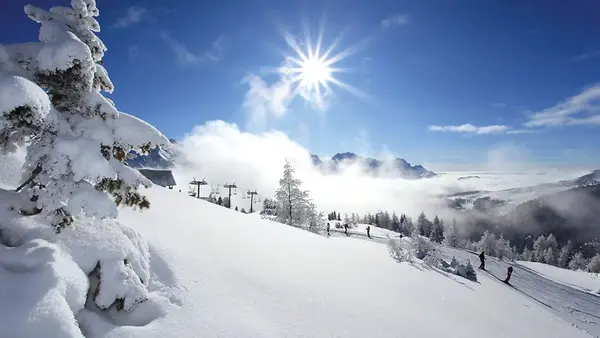 Pista da sci innevata con sciatori, impianti di risalita e sole splendente sulle montagne