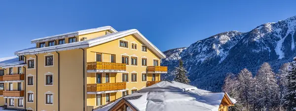 Facciata gialla dell'hotel con balconi in legno e tetto innevato tra le montagne delle Dolomiti