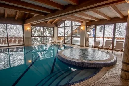 Piscina interna con vasca idromassaggio e ampie vetrate affacciate sul paesaggio innevato