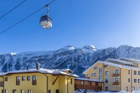 Cabinovia sopra gli edifici dell'hotel innevati con montagne e cielo azzurro