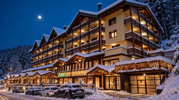 Vista notturna dell'Hotel Armon innevato con luna e abeti circostanti