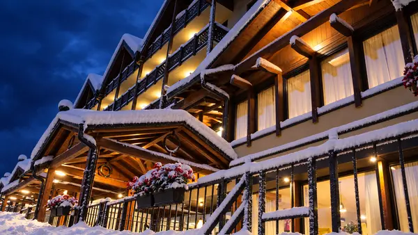Dettaglio della facciata dell'hotel con balconi in legno innevati e fioriere illuminate al crepuscolo